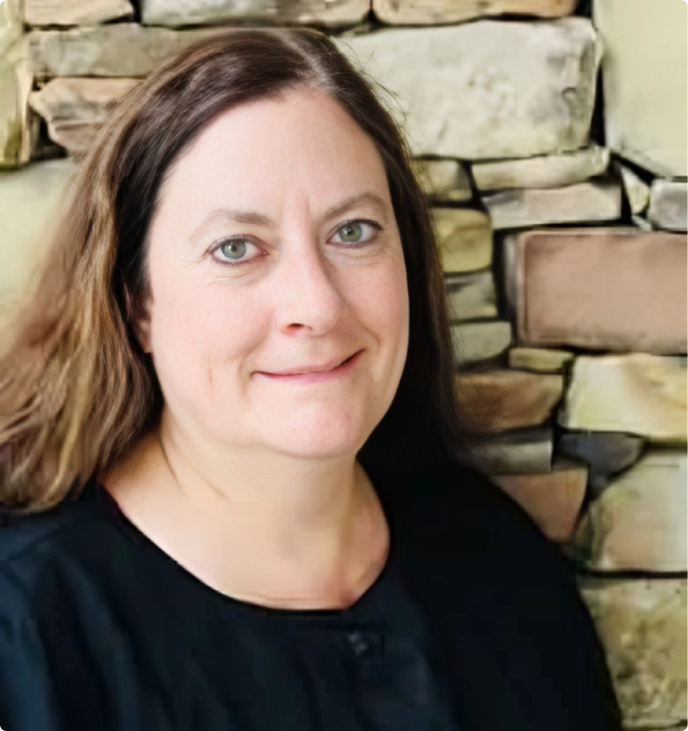 Professional headshot of a woman smiling at camera against stone brick background.