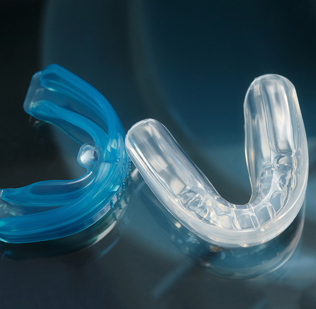Two custom mouth guards, one blue and one clear, displayed on dark surface.