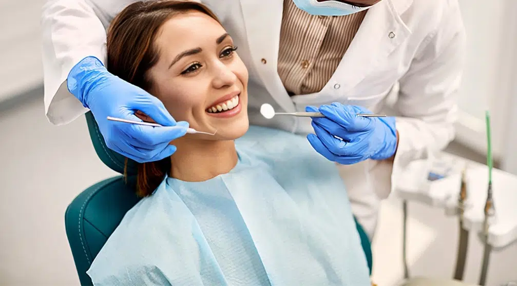 Female patient receiving dental examination from dentist wearing blue gloves in clinical office setting.