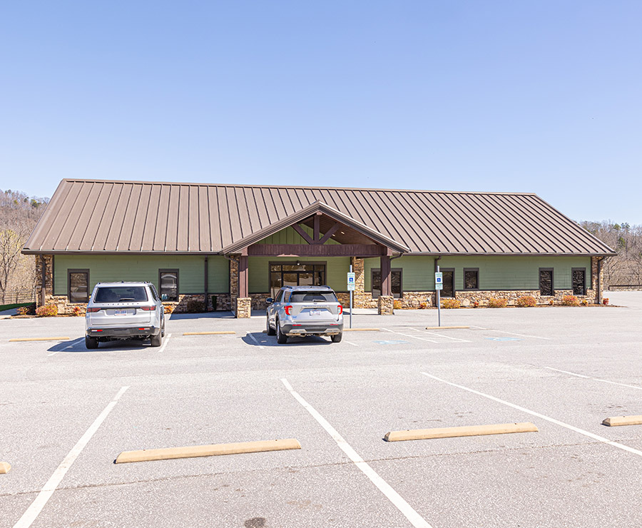 Modern dental office building with metal roof, parking lot, and two vehicles parked outside.